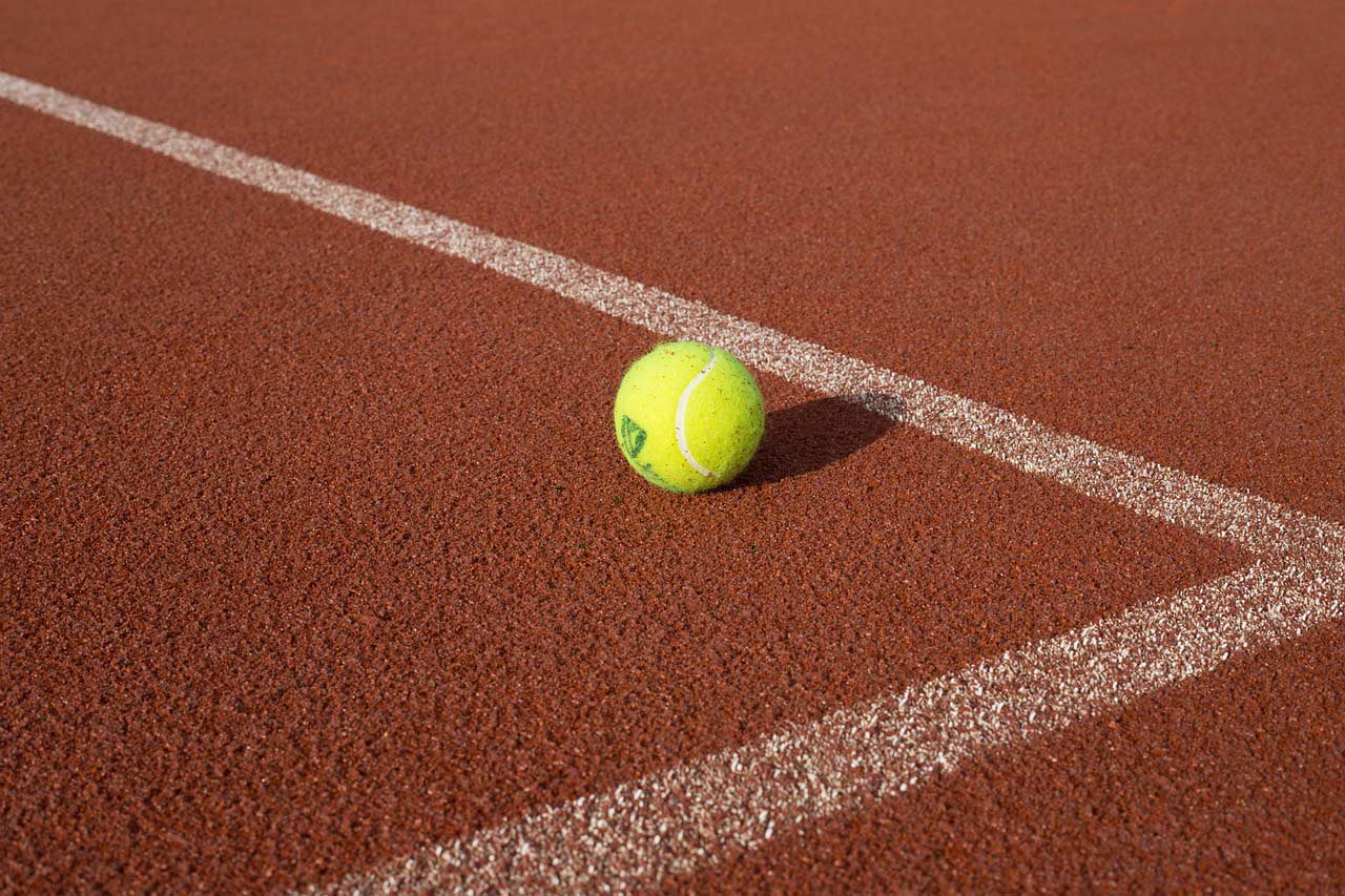 balle de tennis posée sur un court de tennis en bitume orangé