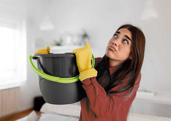 Femme tenant un seau sous une fuite d'eau au plafond