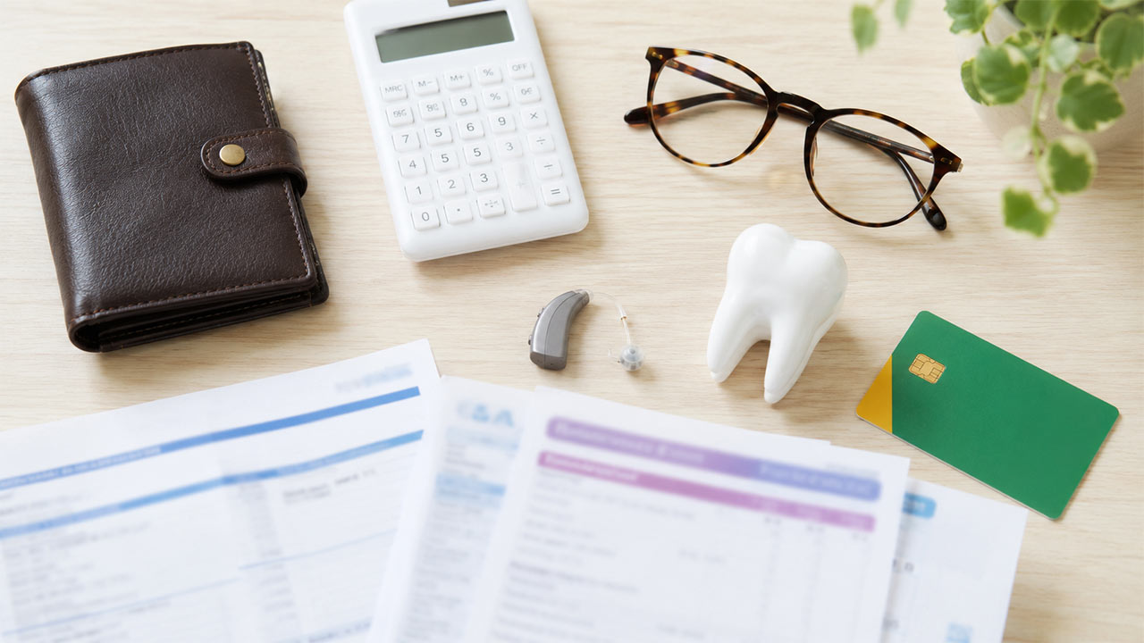 Table avec portefeuille, calculatrice, lunettes, aide auditive, dent et documents floutés pour comparer une mutuelle santé