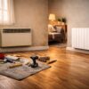 Photo d’un salon français en rénovation, avec un ancien convecteur électrique mural à gauche et un radiateur moderne à droite, outils de bricolage au sol