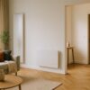 Salon contemporain lumineux, grande baie vitrée, radiateur à inertie design sur un mur intérieur et panneau rayonnant fin dans l’entrée adjacente, ambiance chaleureuse d’hiver, matériaux bois et textile,